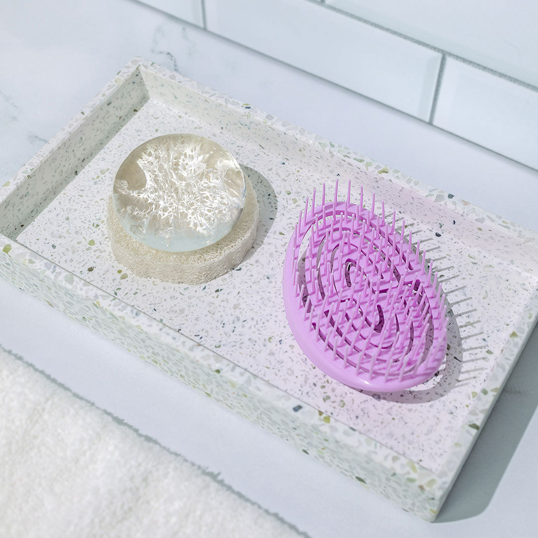 Crystal Clear Head-To-Toe Cleansing Soap on top of our Natural Loofah Soap Dish next to a Scalp Massager, pictured on a vanity tray with a white subway tile background.